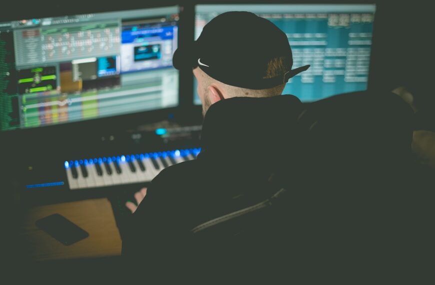 Bilde av en mann som lager musikk foran 2 pc skjermer og et keyboard